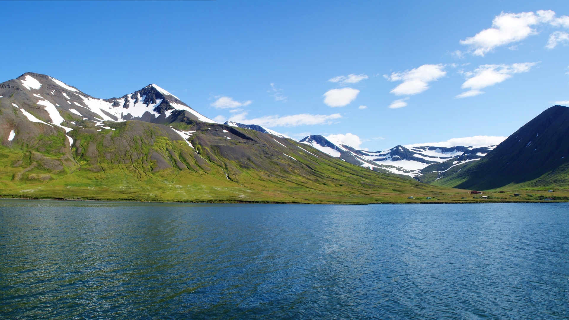 A panoramic view of Skagafjörður's eastern coastline in Northern Iceland, featuring lush green hills and snowy mountains under a clear blue sky.