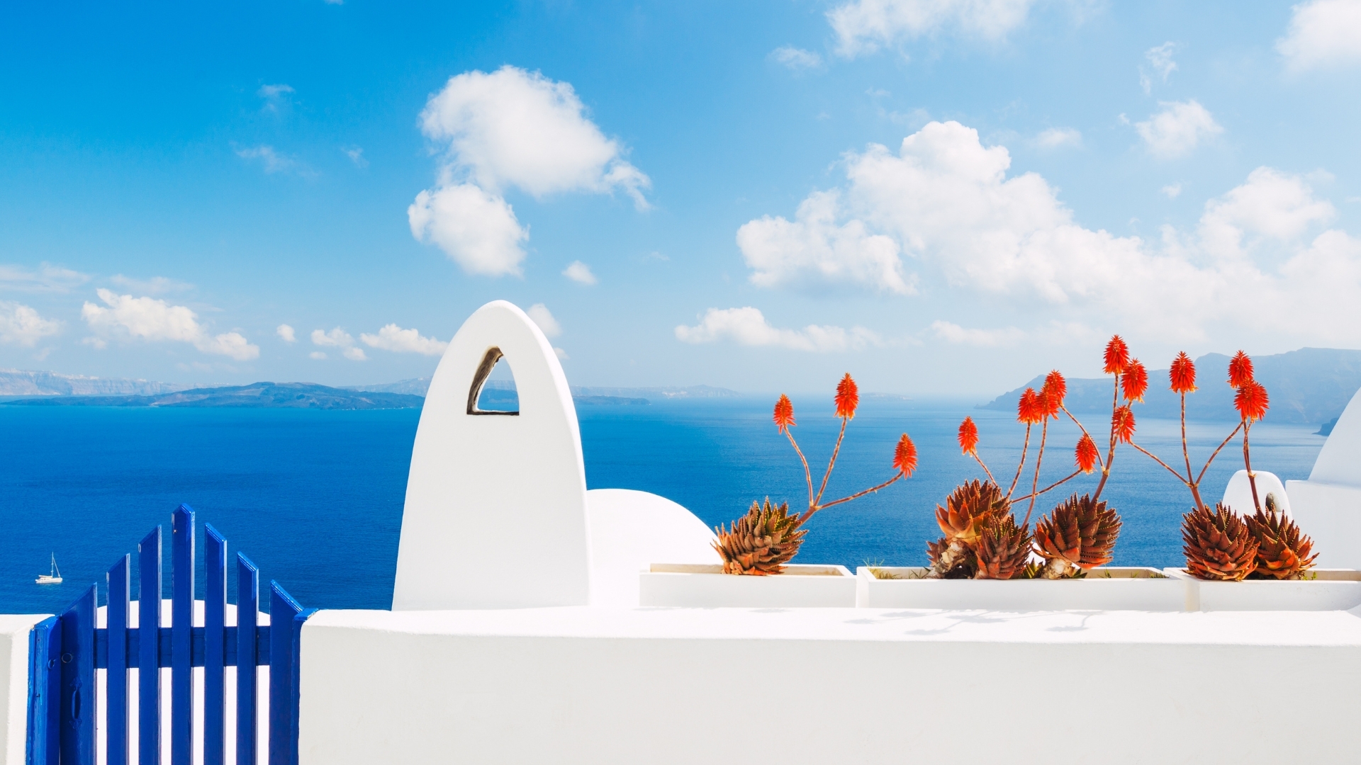 The image depicts a beautiful view of Santorini, Greece, featuring whitewashed buildings with a blue gate and vibrant red flowers in pots, set against a backdrop of the deep blue sea and a clear sky with fluffy clouds.