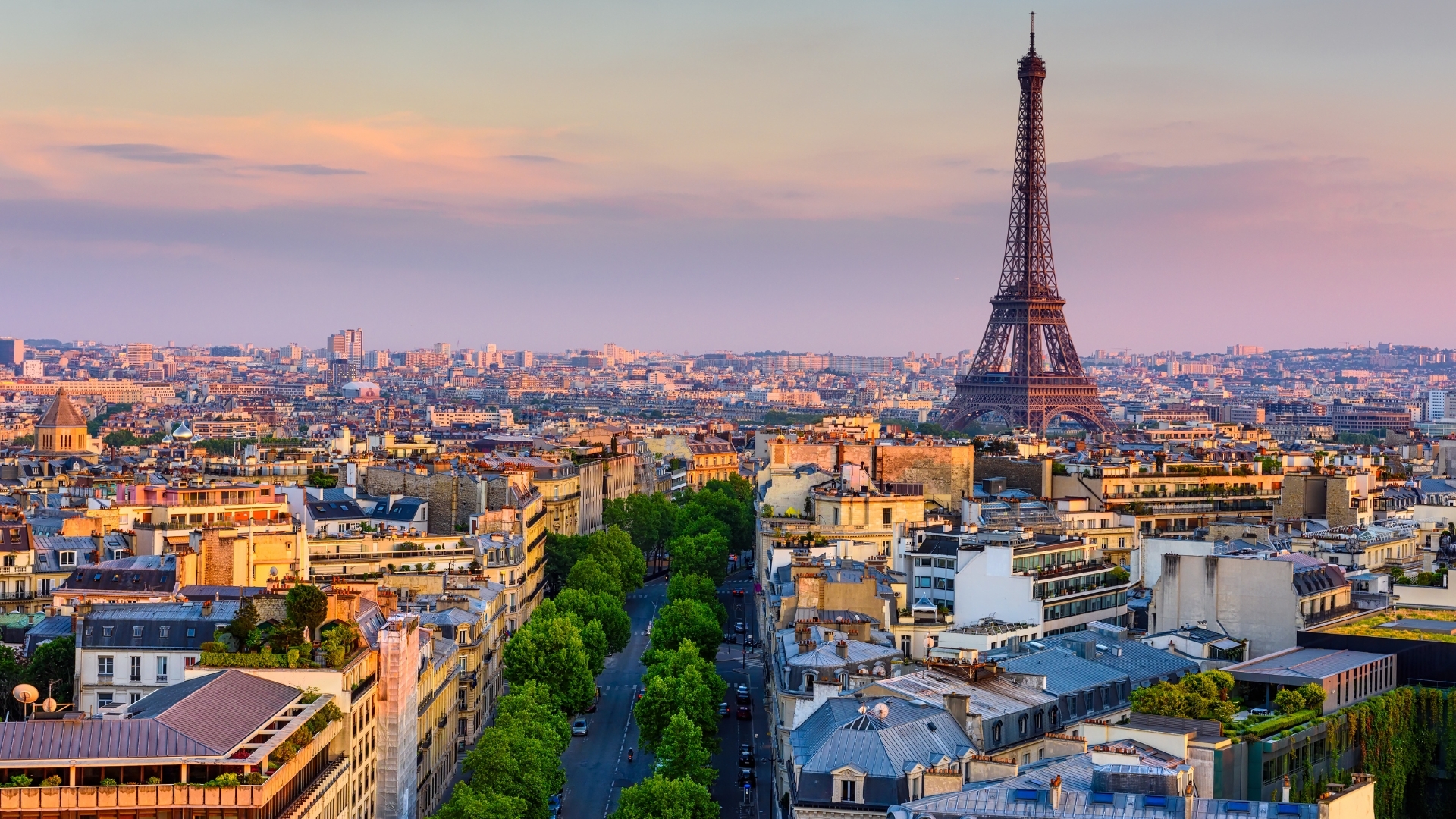 The image shows a panoramic view of Paris, prominently featuring the Eiffel Tower against a backdrop of the city skyline during sunset. The scene captures the beautiful architecture of Parisian buildings and tree-lined streets, creating a picturesque and romantic atmosphere.