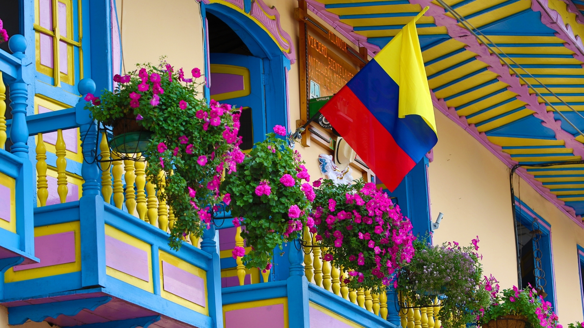 The image showcases colorful colonial balconies in Colombia, adorned with vibrant flowers and the Colombian flag, reflecting the country's rich cultural heritage and lively architecture.